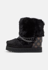 Bottine en fausse fourrure noire avec un talon compensé, des embellissements en chaîne et un détail en cuir à motif à l'arrière.