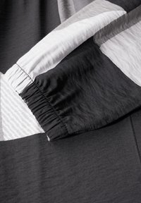 Tissu noir, blanc et gris avec des textures variées et des motifs géométriques. L'ourlet est froncé pour un ajustement élastique. Matériau doux et léger.