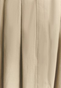 Bež tkanina s teksturiranim ribljim uzorkom. Sadrži oštre nabore i glatku završnu obradu. Dizajnirana za tečan, strukturiran izgled.