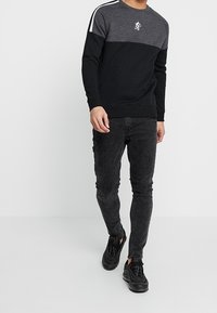 Felpa a maniche lunghe grigia e nera con dettaglio a righe sulle spalle e logo, abbinata a jeans neri slim e sneakers nere.