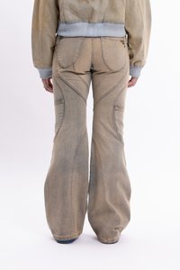 Izblijedjeli bež trapezasti traperice s teksturiranim završetkom, s zakrivljenim šavovima, bočnim džepovima i blago nošenim izgledom.