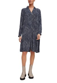 Mörkblå klänning med långa ärmar, krage och abstrakta vita mönster. Matchad med ljusgrå vävda ankelskor på en tjock svart sula.