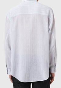 Vaaleansininen, puoliksi läpikuultava pitkähihainen paita, jossa on teksturoitu, ribattu muotoilu. Ominaisuuksia ovat klassinen kaulus ja napitettu hihansuu.