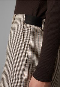 Korkeavyötäröiset, ruudulliset housut, joissa on vaaleankeltaisia, ruskeita ja valkoisia värejä; sisältää sivutaskut ja mustan vyötärönauhan.