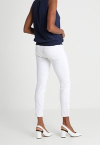 Marinblå ärmlös topp, vita smala jeans med knappdetaljer vid ankeln och vita högklackade pumps med svart klädd klack.