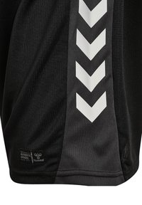 Pantaloni sportivi neri con strisce verticali grigio scuro, caratterizzati da cinque chevron bianchi rivolti verso il basso e un piccolo etichetta con la scritta "Authentic Apparel hummel."