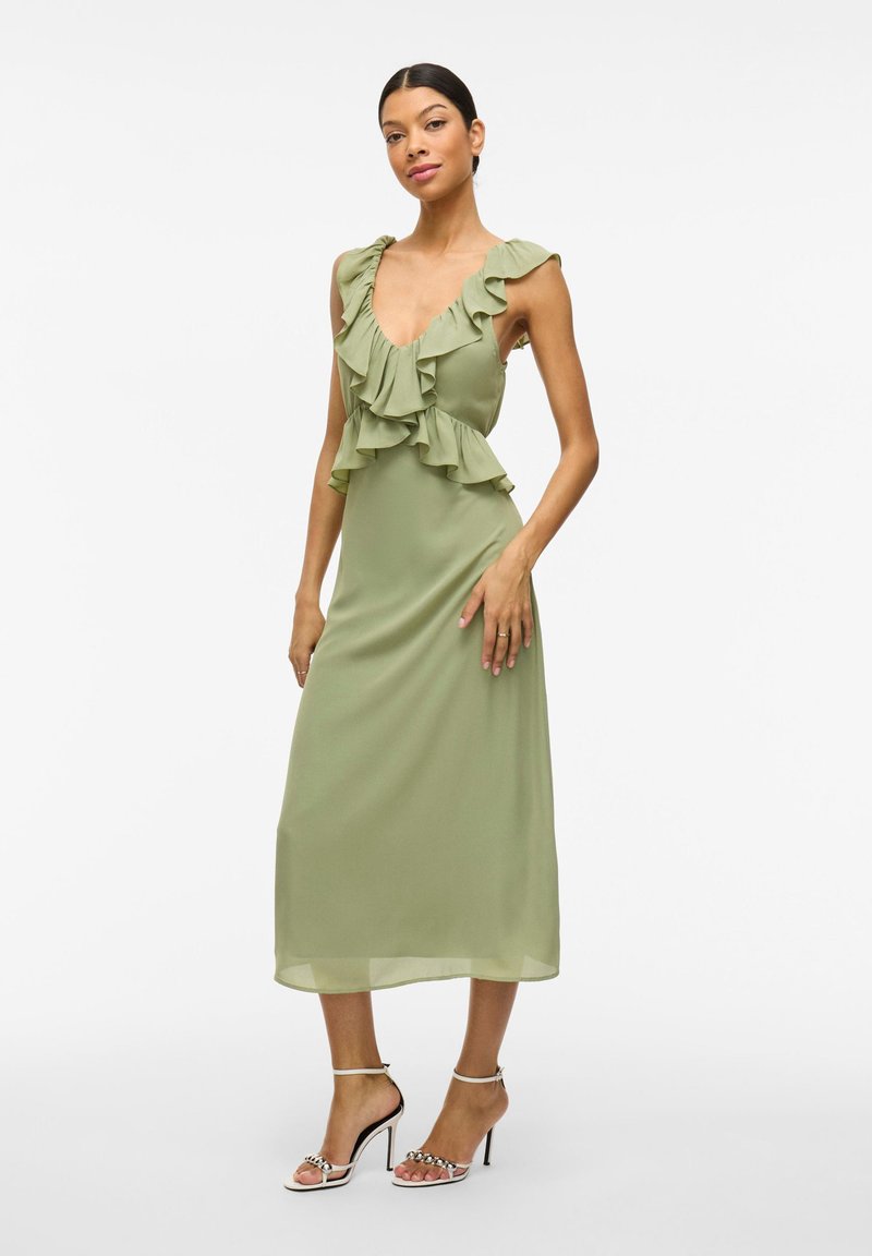 Rochie midi verde, fără mâneci, cu detalii fluturate la decolteu și talie. Material neted cu o siluetă fluidă, în formă de A.