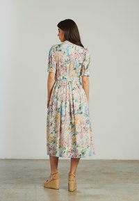 Abito midi floreale in tonalità pastello realizzato in tessuto leggero. Presenta maniche a sbuffo corte, vita segnata da una cintura e una gonna fluida.