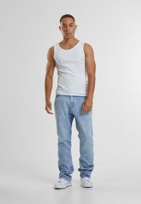 Hvit tanktopp, lyseblå jeans og hvite sneakers. Modellen står foran en lys bakgrunn og viser frem avslappet, ledig antrekk.