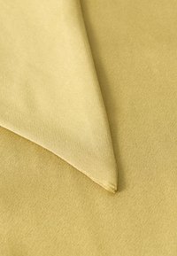 Primo piano di tessuto giallo senape morbido, piegato, con una texture liscia e un motivo di intreccio sottile.