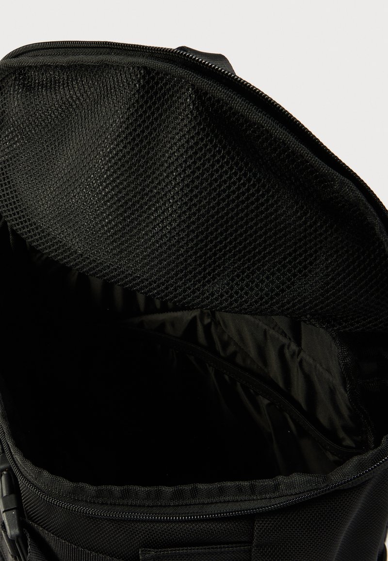 Black backpack interior featuring a textured mesh pocket and a smooth fabric lining. Zipper closure and spacious, organized compartments.