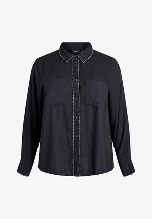 Črna srajca s dolgimi rokavi in dvema sprednjima žepoma. Ima kontrastne bele šive na ovratniku in zadrgi.