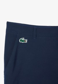 Pantalones cortos azul marino hechos de un tejido suave, con un vibrante logo de cocodrilo de Lacoste en verde y rojo en el lado izquierdo.
