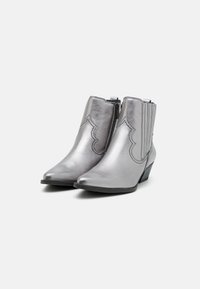 Botines de cuero plateado hasta el tobillo con punta afilada, acentos ondulados, cierre de cremallera y un tacón bajo apilado. Textura suave y diseño elegante.