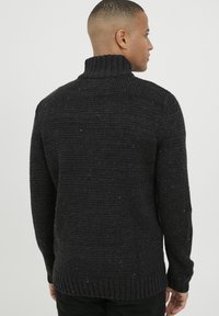 Suéter de punto gris oscuro con un alto cuello acanalado, que presenta un patrón texturizado y motas desiguales de hilo, puños acanalados y dobladillo.