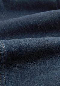 Tissu en denim bleu foncé avec texture de tissage diagonale visible et vue rapprochée de couches pliées et d'une couture cousue.
