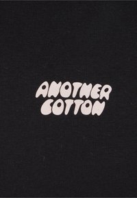 Tessuto di cotone nero con la scritta "ANOTHER COTTON" in lettere bianche, giocose e arrotondate. Texture liscia e design minimalista.