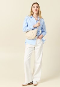 Ljusblå knäppt skjorta, vita vida byxor, beige axelväska med mjuk textur och vita sneakers med svarta ränder.
