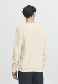 Maglione a coste di colore crema con scollatura rotonda e maniche lunghe, caratterizzato da un tessuto testurizzato e polsini e orlo elasticizzati.