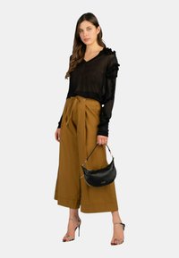 Top nero trasparente a maniche lunghe con dettagli arricciati, abbinato a pantaloni giallo senape a vita alta e gamba larga, insieme a una borsa nera. Tacchi con cinturino.