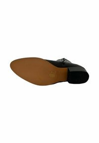 Zapato de piel negra con punta redondeada y tacón cuadrado bajo. La suela es marrón con una textura antideslizante. Presenta acentos decorativos en la parte superior.