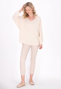 Pulover supradimensionat de culoare bej deschis, cu gât în V, material texturat și mâneci lungi, asortat cu pantaloni bej strâmți și încălțăminte deschisă.
