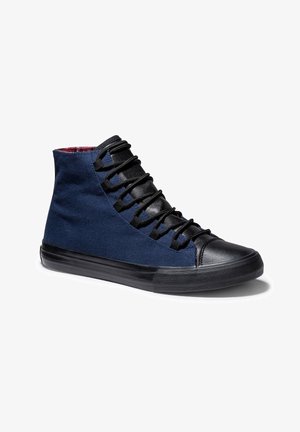 Zapatilla deportiva de caña alta con paneles laterales de tela azul marino, puntera y lengüeta de cuero negro, cordones negros y suela de goma negra.