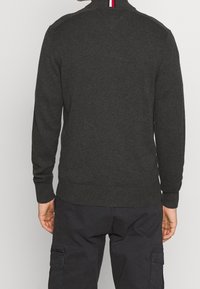 Ciemnoszary dzianinowy sweter z długimi rękawami, wysokim kołnierzem, prążkowanym dołem i czerwono-białym akcentem na szwie przy szyi, o fakturowanym wykończeniu.