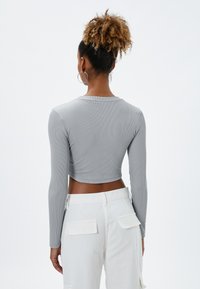 Top gris corto de manga larga con textura acanalada, con un escote redondeado. Combinado con pantalones cargo blancos con bolsillos de parche.
