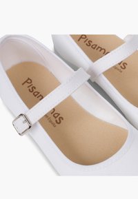 Pantofi Mary Jane din pânză albă, cu o curea subțire și cataramă argintie. Interior moale de culoare bej cu numele brandului imprimat. Talpă plată.