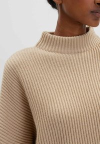 Beige gestreifter Pullover mit hohem Kragen, der ein strukturiertes Strickmuster und einen weichen, leichten Stoff aufweist. Nahaufnahme, die die Nähte betont.