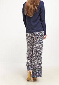 Haut à manches longues bleu marine associé à un pantalon palazzo à motifs floraux en bleu marine, rose et crème, terminé par une ceinture texturée.