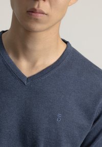 Suéter azul marino con diseño de escote en V, hecho de un material suave y texturizado. Presenta un pequeño logotipo bordado en el lado izquierdo.