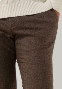 Brown checkered trousers made of textured fabric. Features a fitted design with visible stitching and a slight sheen.