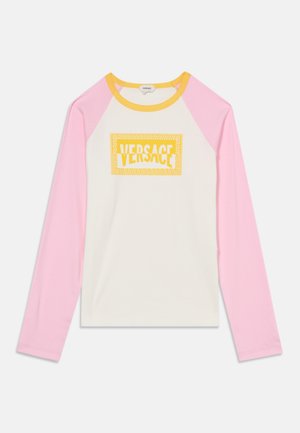Chemise à manches longues avec manches raglan roses, corps blanc, col jaune et logo Versace jaune centré sur la poitrine.