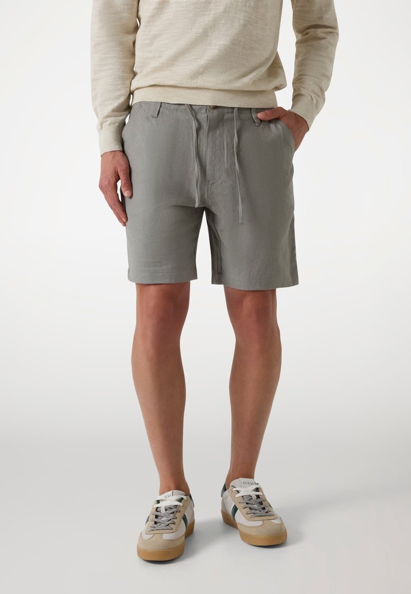 Gray shorts with a drawstring waist and side pockets, made from a soft, lightweight fabric; paired with beige sneakers featuring green accents.