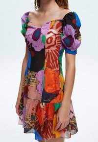 Robe à manches courtes avec des motifs floraux vibrants en rose, vert, orange et bleu. Confectionnée en tissu léger avec une silhouette fluide.