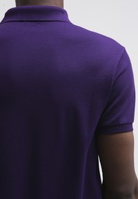 Lila polo skjorta med texturerad tyg, korta ärmar och en klassisk krage. Baksidan har minimal sömnad och rena linjer.