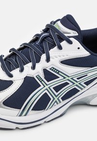 Marinblå och vit träningsskor med mesh-material och syntetiska överlägg, med mörka snören och en ljusgrönrandig logotyp på sidan.