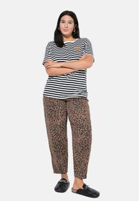 Camiseta de rayas blancas y negras con un detalle de corazón, combinada con pantalones de leopardo marrón y zapatos negros tipo slip-on.