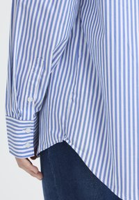 Light blue and white striped shirt with a relaxed fit, button cuffs, and a curved hem; made of smooth, lightweight fabric.