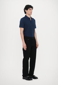 Navy short-sleeve button-up shirt, black straight-leg trousers, black shoes with gold hardware accents. Minimalist design and smooth texture.