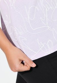 Camiseta lila con un dibujo abstracto en línea blanca, combinada con pantalones negros. El diseño enfatiza una textura suave y un ajuste relajado.