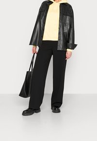 Giubbotto di pelle nera, felpa gialla con cappuccio, pantaloni neri a gamba larga, stivali neri chunky e borsa a tracolla nera. Texture liscia, design a strati.