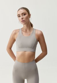 Soutien-gorge de sport gris clair en tissu extensible avec un encolure en scoop et des bretelles larges, associé à un legging taille haute assorti.