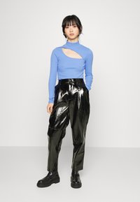 Top azul de manga longa com detalhe recortado, combinado com calças pregueadas pretas brilhantes e botas pretas robustas. Design simples e moderno.