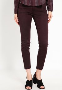 Vínové úzké džíny s přiléhavým střihem a hladkou texturou, doplněné černými sandály s otevřenou špičkou na podpatku s robustním podpatkem.