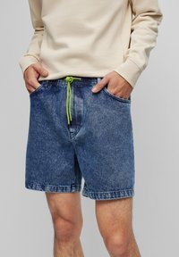 Džínové šortky v tmavě modré barvě s vyšisovaným vzhledem. Mají elastický pas s zelenou šňůrkou, boční kapsy a volný střih.