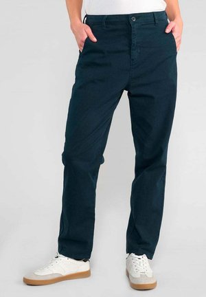 Dunkelblaue Baumwollhose mit geradem Bein, Knopfverschluss und Seitentaschen, kombiniert mit weißen Sneakers mit beigen Sohlen.