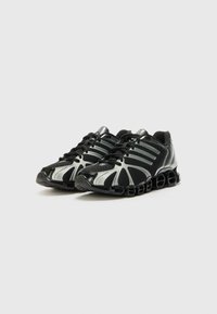 Baskets de sport noires et argentées avec une tige en maille, de multiples trous de ventilation et un design de semelle segmentée distinct pour un meilleur amorti.